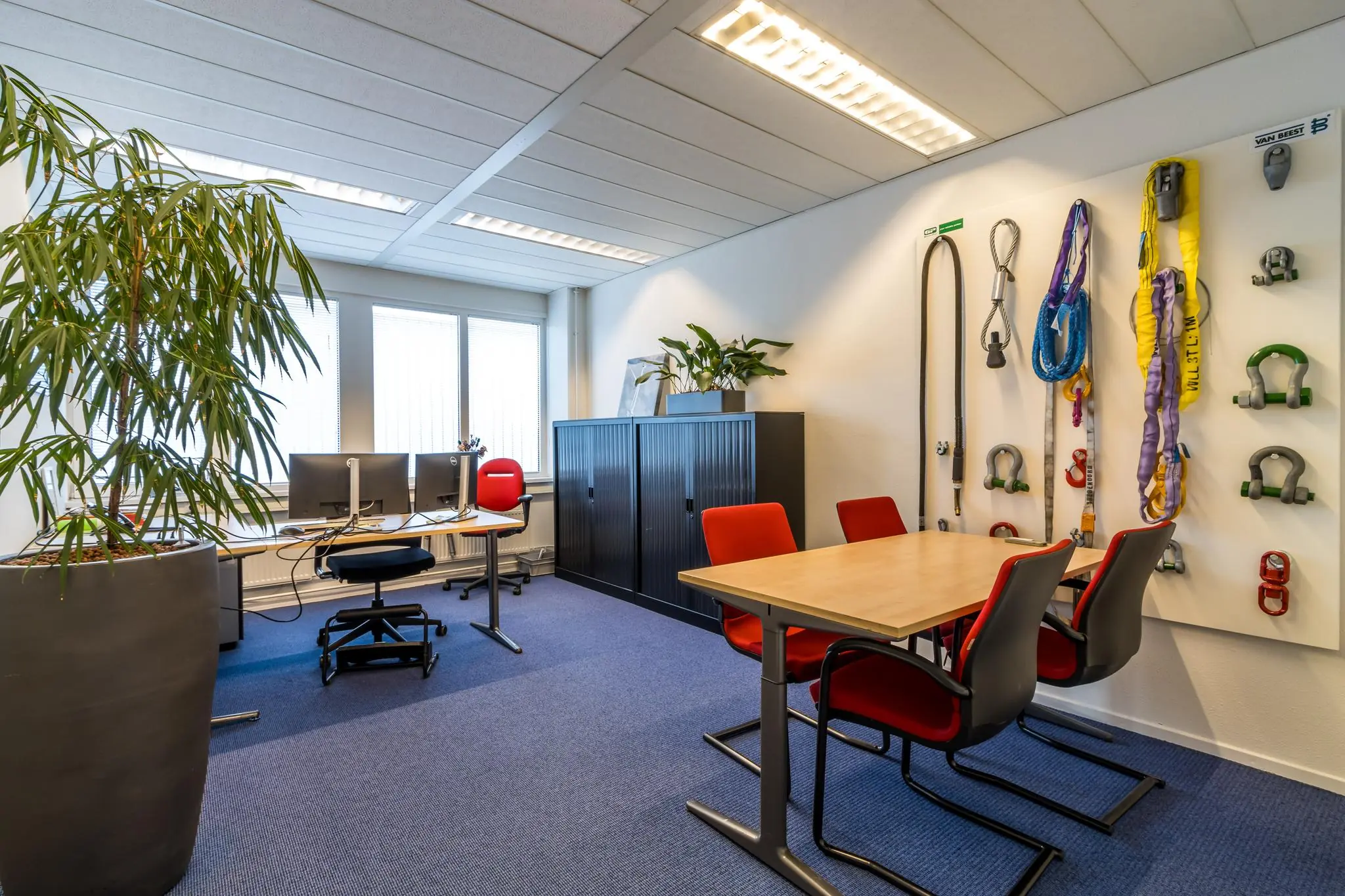 Kantoorruimte aan de Savannahweg met werkplekken, vergadertafel en wand met hijsmaterialen.