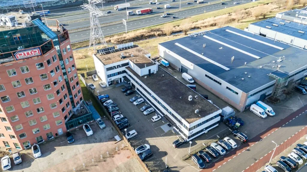 Luchtfoto van kantoren en bedrijfsgebouwen aan de Savannahweg in Utrecht, met zicht op parkeerplaatsen en de snelweg A2 op de achtergrond.