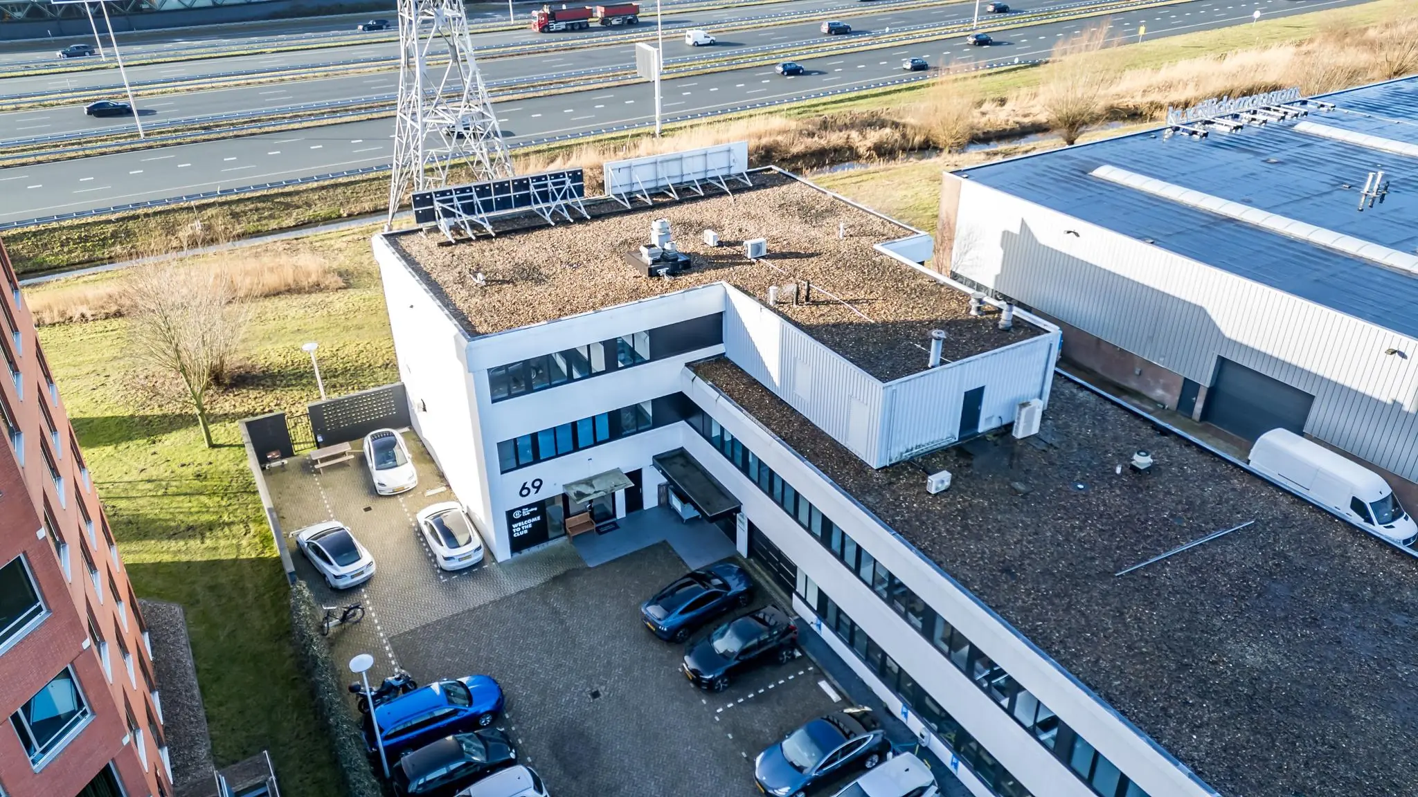 Luchtfoto van een modern bedrijfsgebouw aan de Savannahweg 69 met parkeerplaatsen en snelweg op de achtergrond.