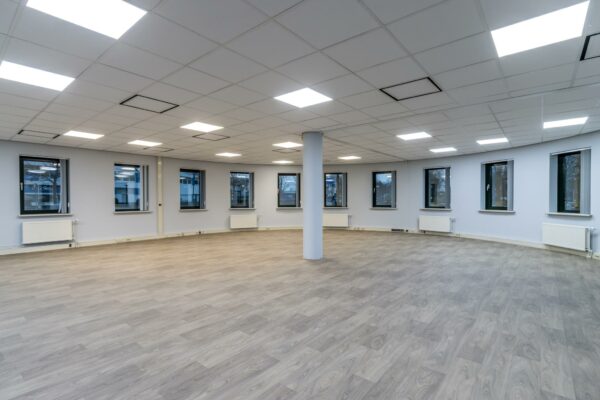 Leeg kantoorpand aan de Koningsweg met lichtgrijze vloer, systeemplafond en meerdere ramen.