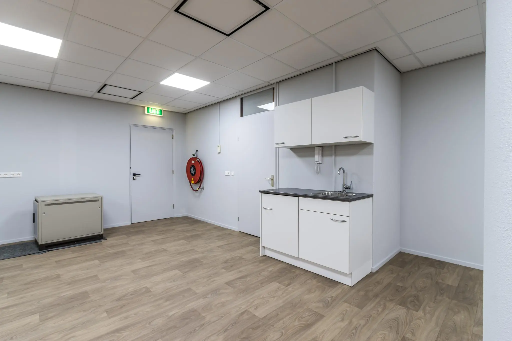 Kleine kitchenette in een lege, modern afgewerkte ruimte aan de Koningsweg met laminaatvloer en brandslanghaspel.
