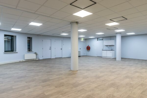 Lege kantoorruimte aan de Koningsweg met lichtgrijze muren, systeemplafond, houtlook vloer en een kleine kitchenette.