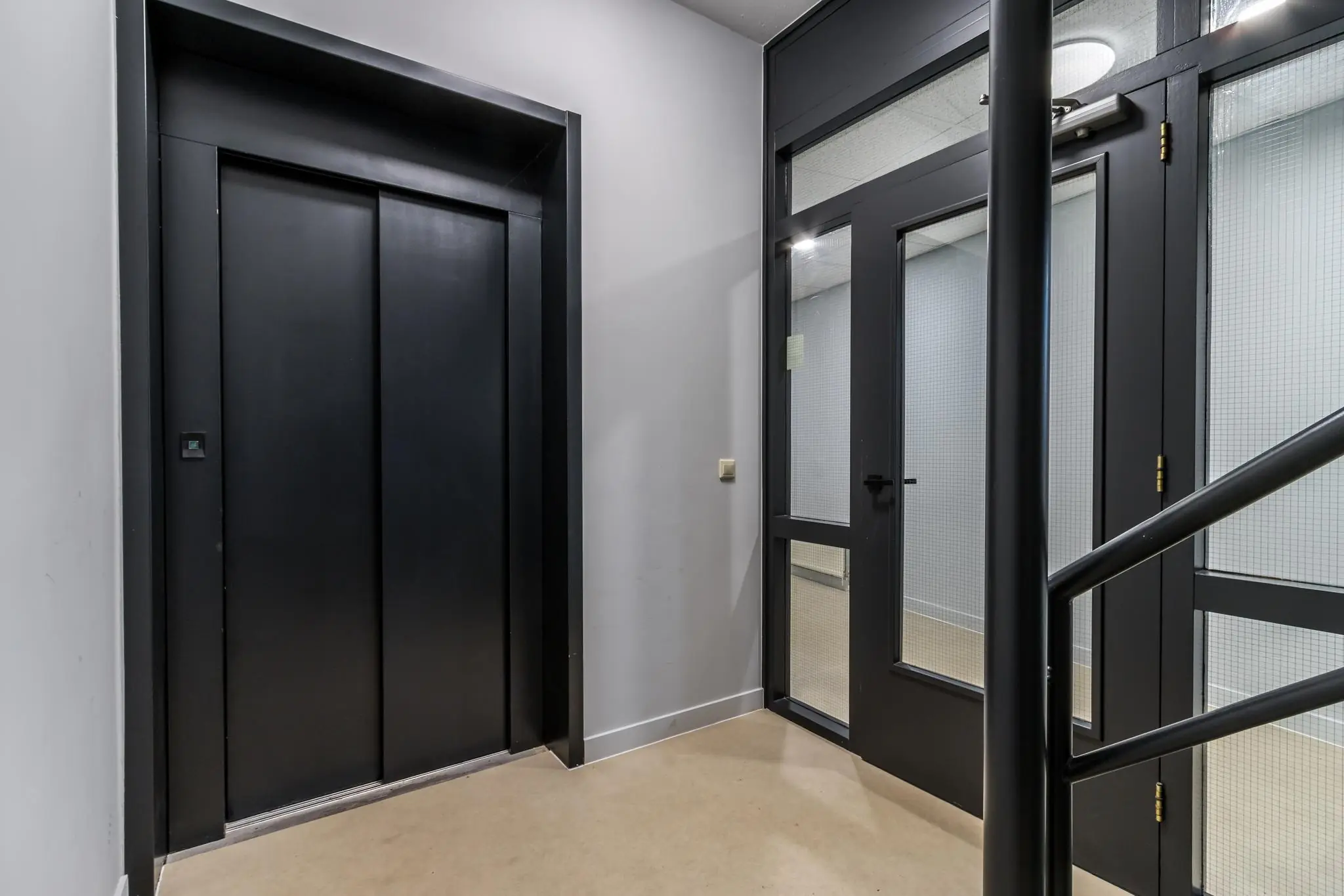 Moderne binnengang met een zwarte liftdeur en glazen deur in een kantoorgebouw aan de Koningsweg.