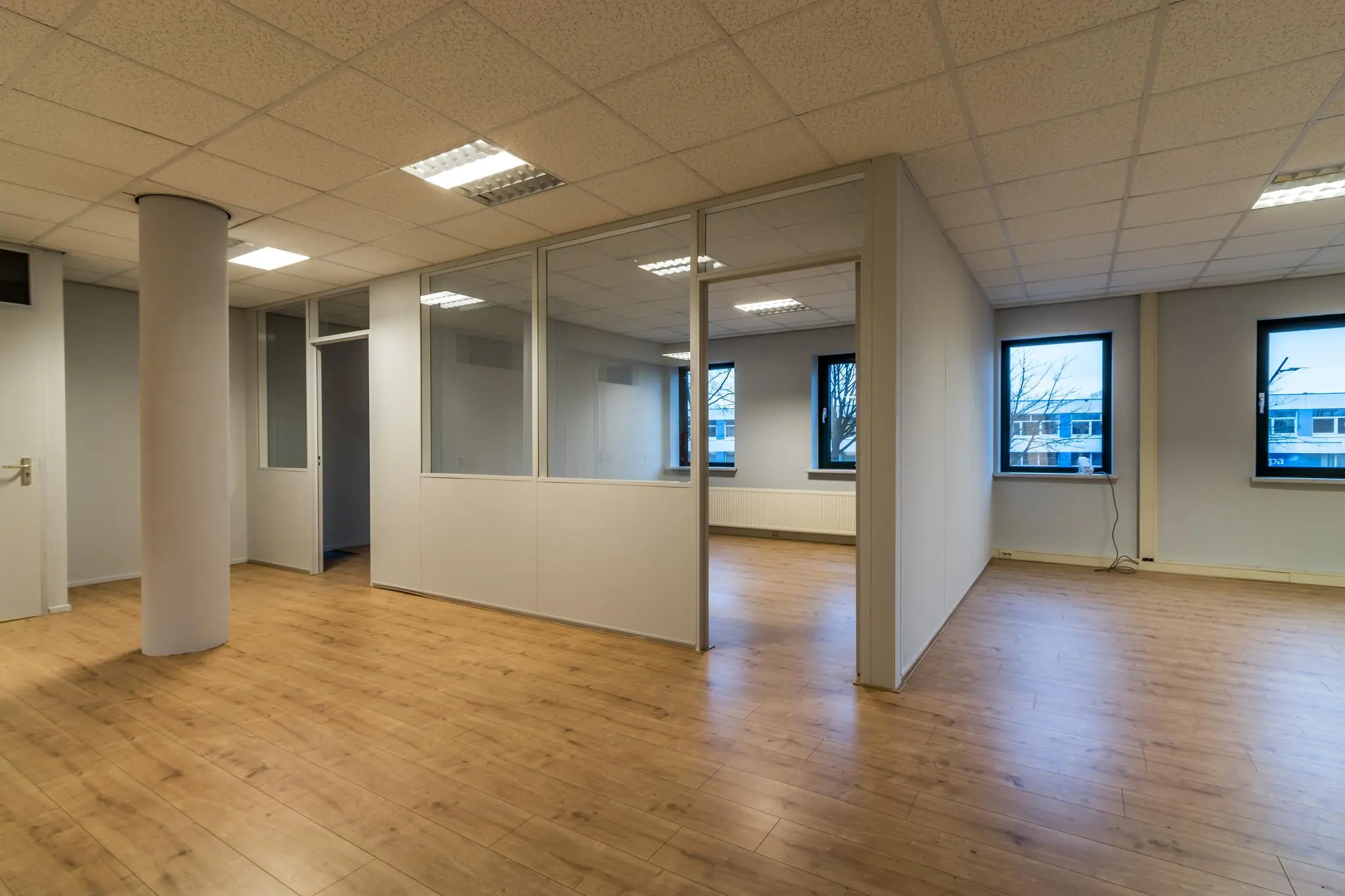 Licht en leeg kantoorpand aan de Koningsweg met houten vloer en glazen scheidingswanden.