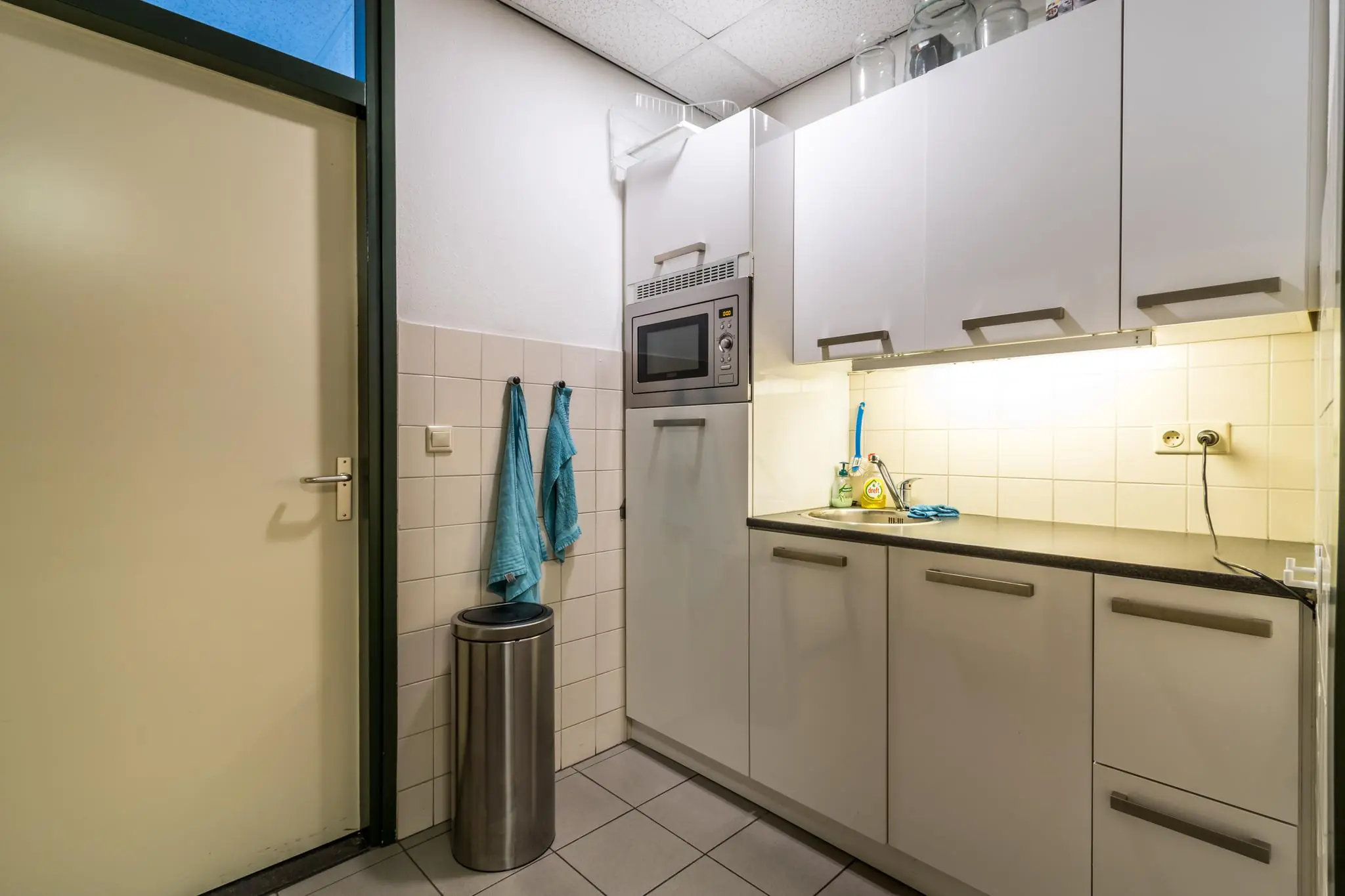 Kleine, functionele keuken aan de Koningsweg met witte kasten, gootsteen en ingebouwde magnetron.