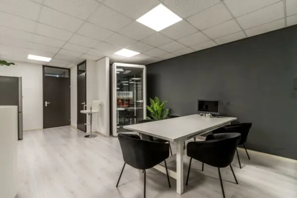 Moderne kantoorruimte aan de Koningsweg met een vergadertafel, zwarte stoelen, een computer en een aparte belcel van 2XCEED.