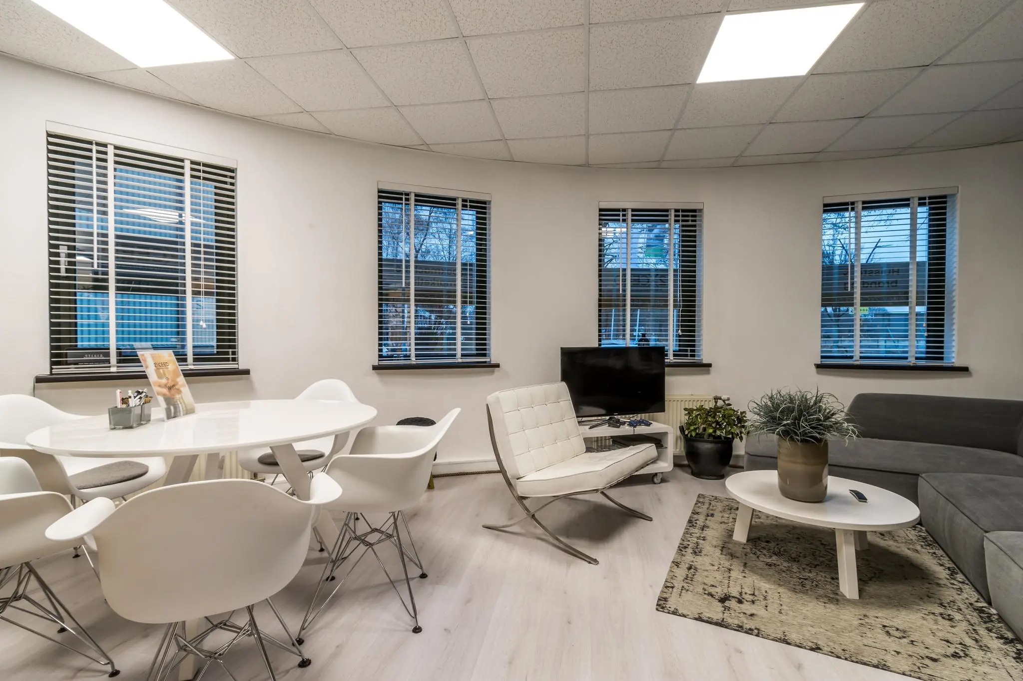 Moderne wachtruimte aan de Koningsweg met witte eettafel, zithoek en vijf ramen met jaloezieën.