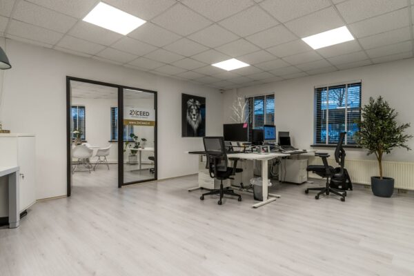 Modern kantoorinterieur aan de Koningsweg met werkplekken, een vergaderruimte en het logo van 2xCEED op de glazen deur.