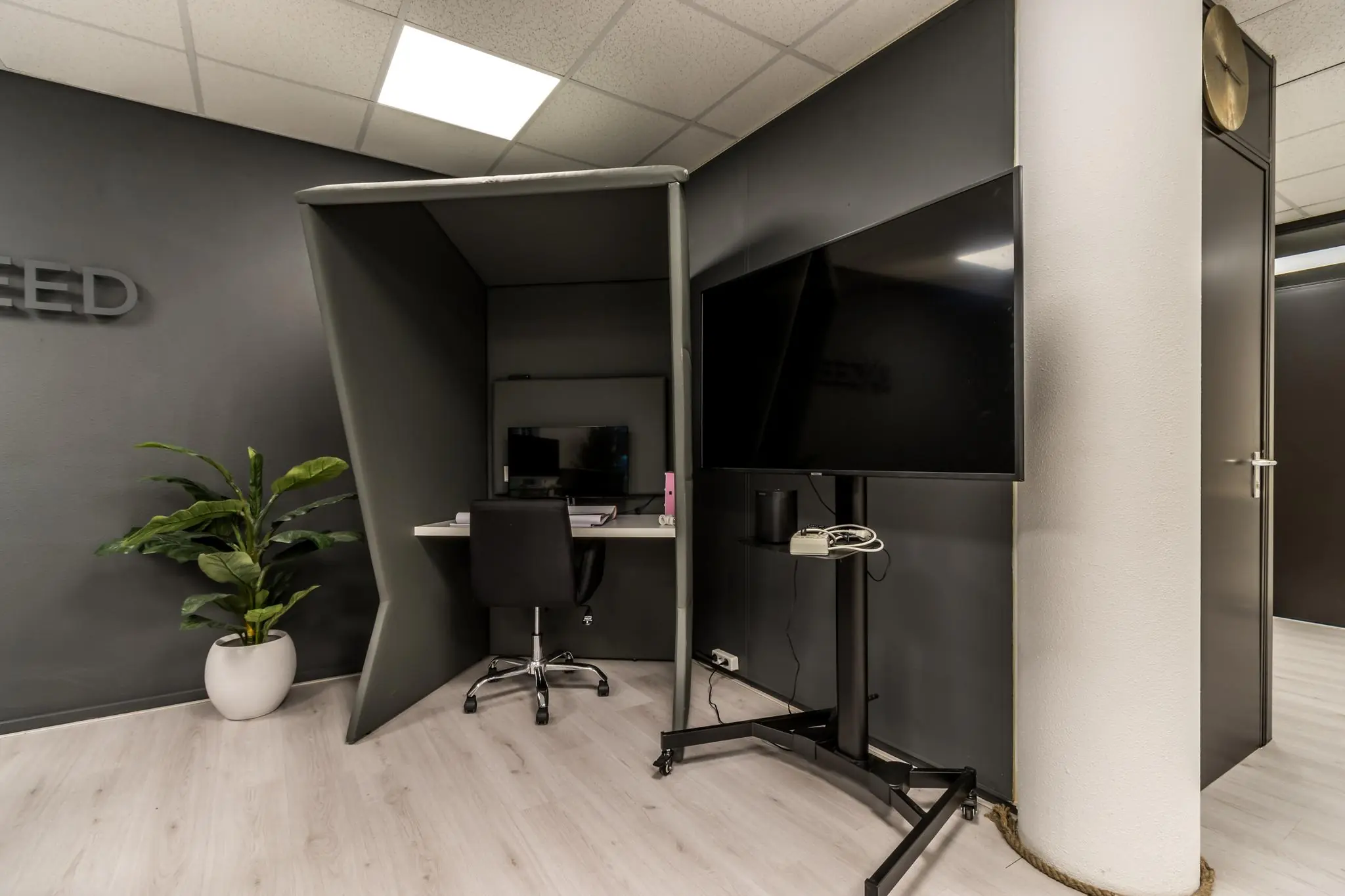 Moderne kantoorruimte met een stille werkplek, bureaustoel, computerscherm en een grote tv op een standaard.