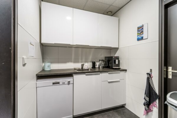 Moderne pantry met witte kasten, een koffiezetapparaat, vaatwasser en spoelbak aan de Koningsweg.