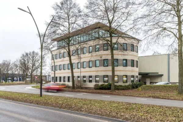 Kantoorgebouw aan de Koningsweg met ronde gevel en omliggende bomen op een bewolkte dag.