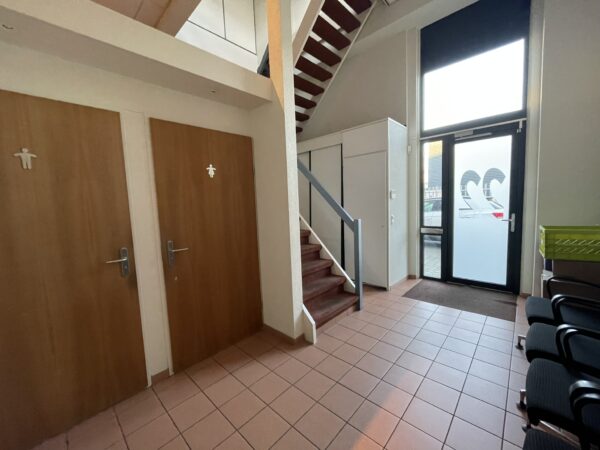 Hal met trap, twee toiletten, wachtruimte en een glazen voordeur met het nummer 22.