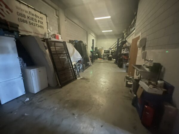 Opslagruimte met stapels matrassen, rekken, apparatuur en een werkblad met gootsteen aan de rechterzijde.
