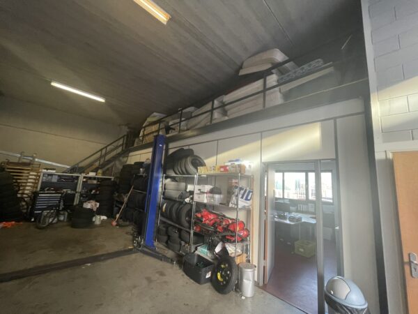 Opslagruimte in een garage met autobanden, een hefbrug en matrassen op een bovenverdieping.
