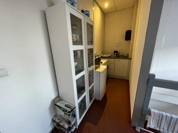 Kleine smalle keuken met witte kasten, servieskast, koelkast en aanrecht met keukengerei.