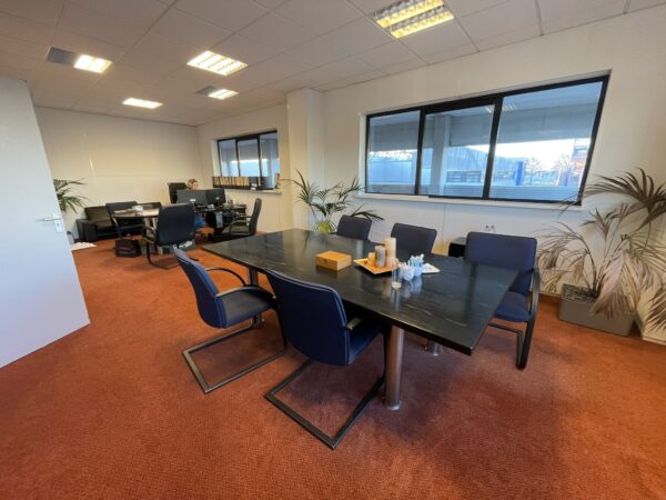 Moderne kantoorruimte met een vergadertafel, bureaus, stoelen en grote ramen met uitzicht naar buiten.