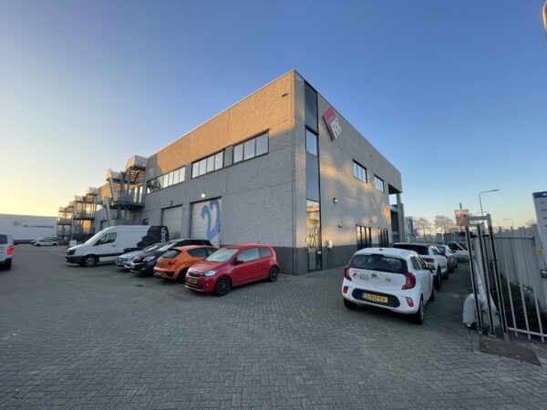 Bedrijventerrein met een modern grijs kantoorpand van IRC en geparkeerde auto's op een zonnige dag.