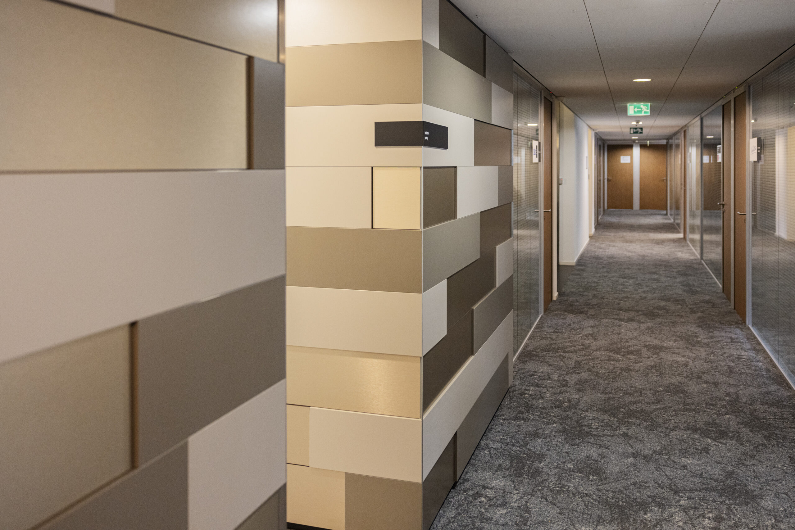 Een moderne gang op een derde verdieping met een geometrisch patroon van beige en witte panelen aan de muur.