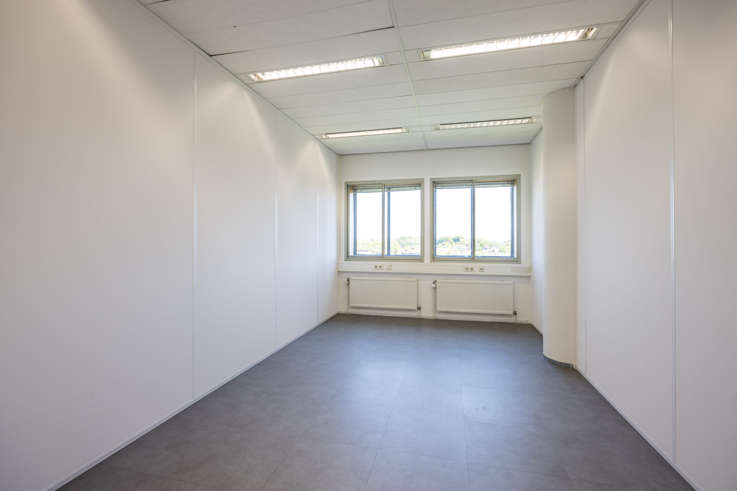 Leeg kantoor met witte muren, grote ramen en grijze tegelvloer bij Element Offices in Utrecht.