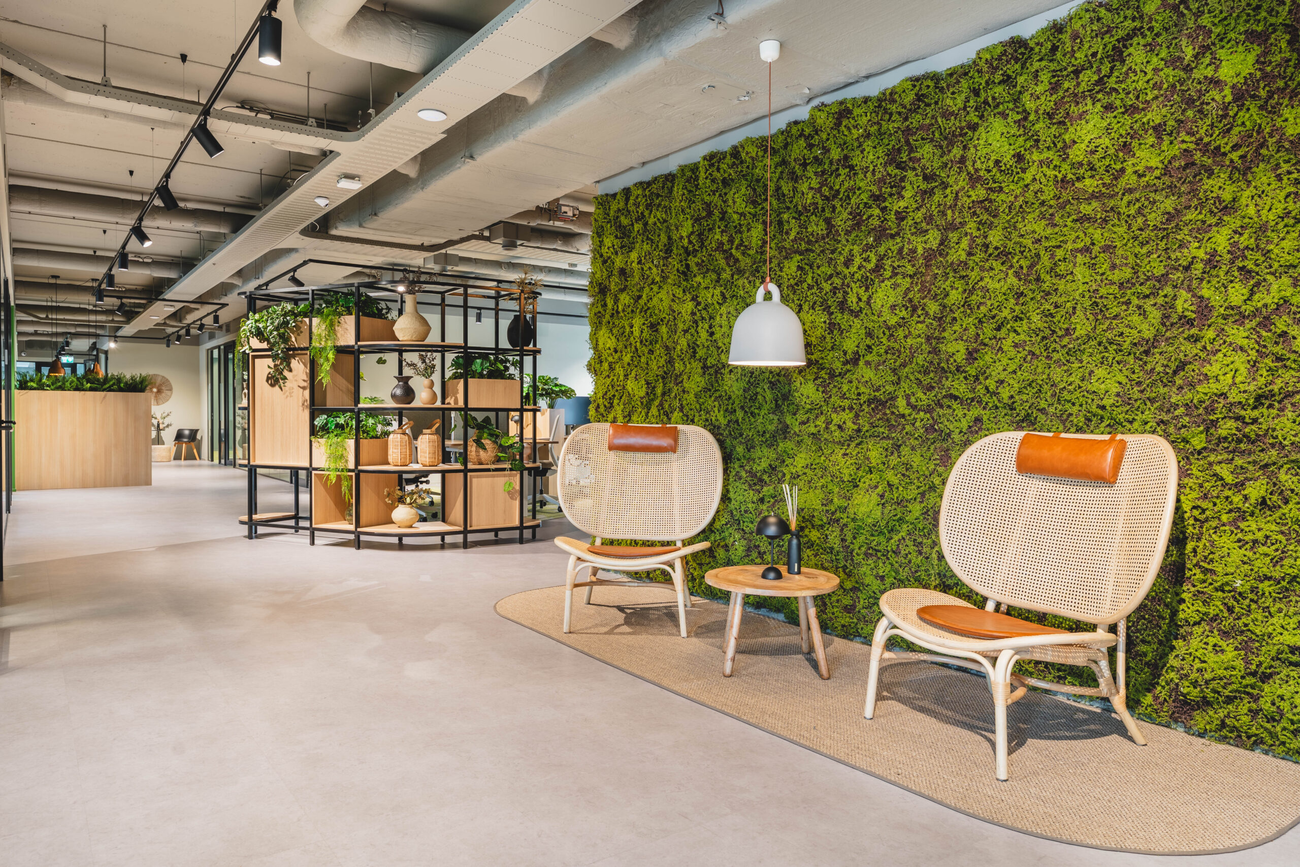 Een moderne kantoorruimte met een groene moswand, rotan stoelen en decoratieve planten in houten rekken.