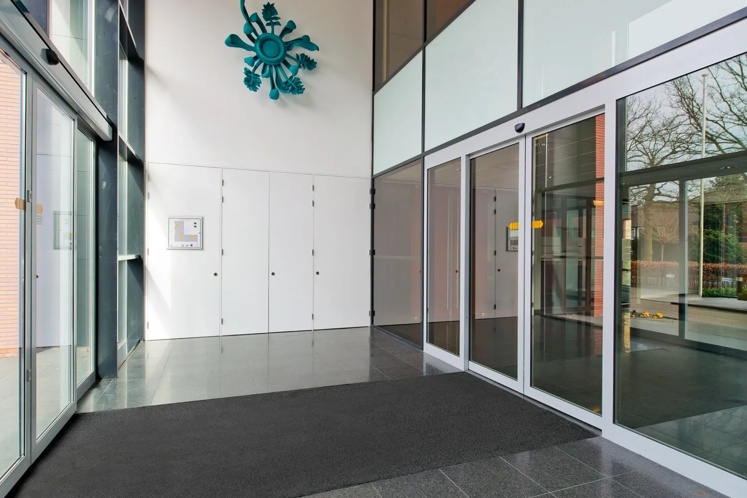 Ingang van een modern kantoorgebouw aan de Groenekanseweg met glazen schuifdeuren, strakke witte muren en een opvallend blauw kunstwerk aan de muur.