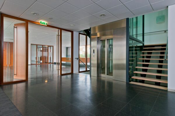 Moderne entreehal aan de Groenekanseweg met glazen deuren, stalen lift en open houten trap.