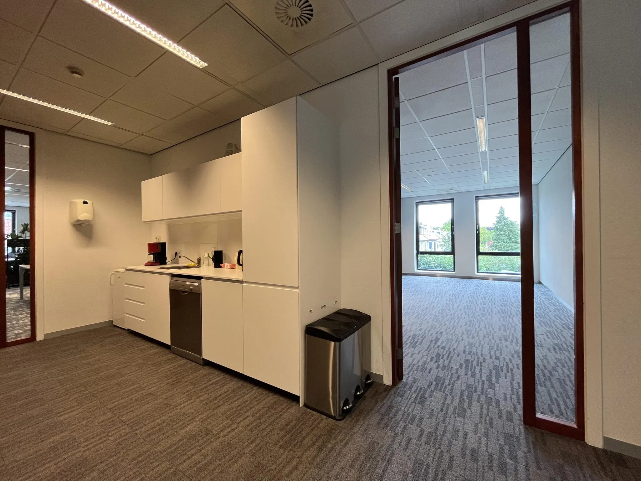 Moderne kantoorpantry aan de Groenekanseweg met uitzicht op een aangrenzend leeg kantoor met grote ramen.