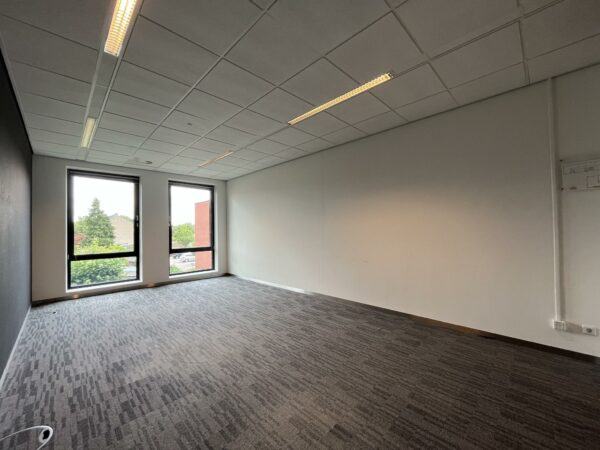 Leeg kantoor met tapijtvloer, systeemplafond en twee ramen met uitzicht op de Groenekanseweg.