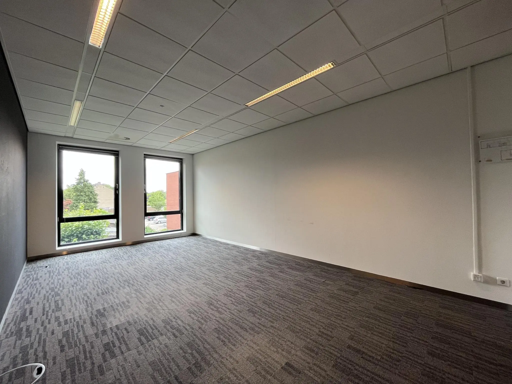Leeg kantoor met tapijtvloer, systeemplafond en twee ramen met uitzicht op de Groenekanseweg.