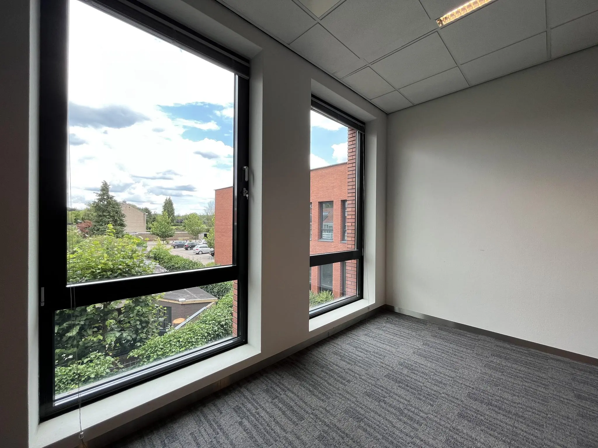 Leeg kantoor met twee grote ramen en uitzicht op de Groenekanseweg en omliggende gebouwen.