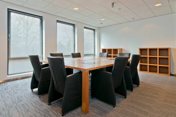 Vergaderruimte aan de Groenekanseweg met een grote houten tafel, zwarte stoelen en open houten kasten.