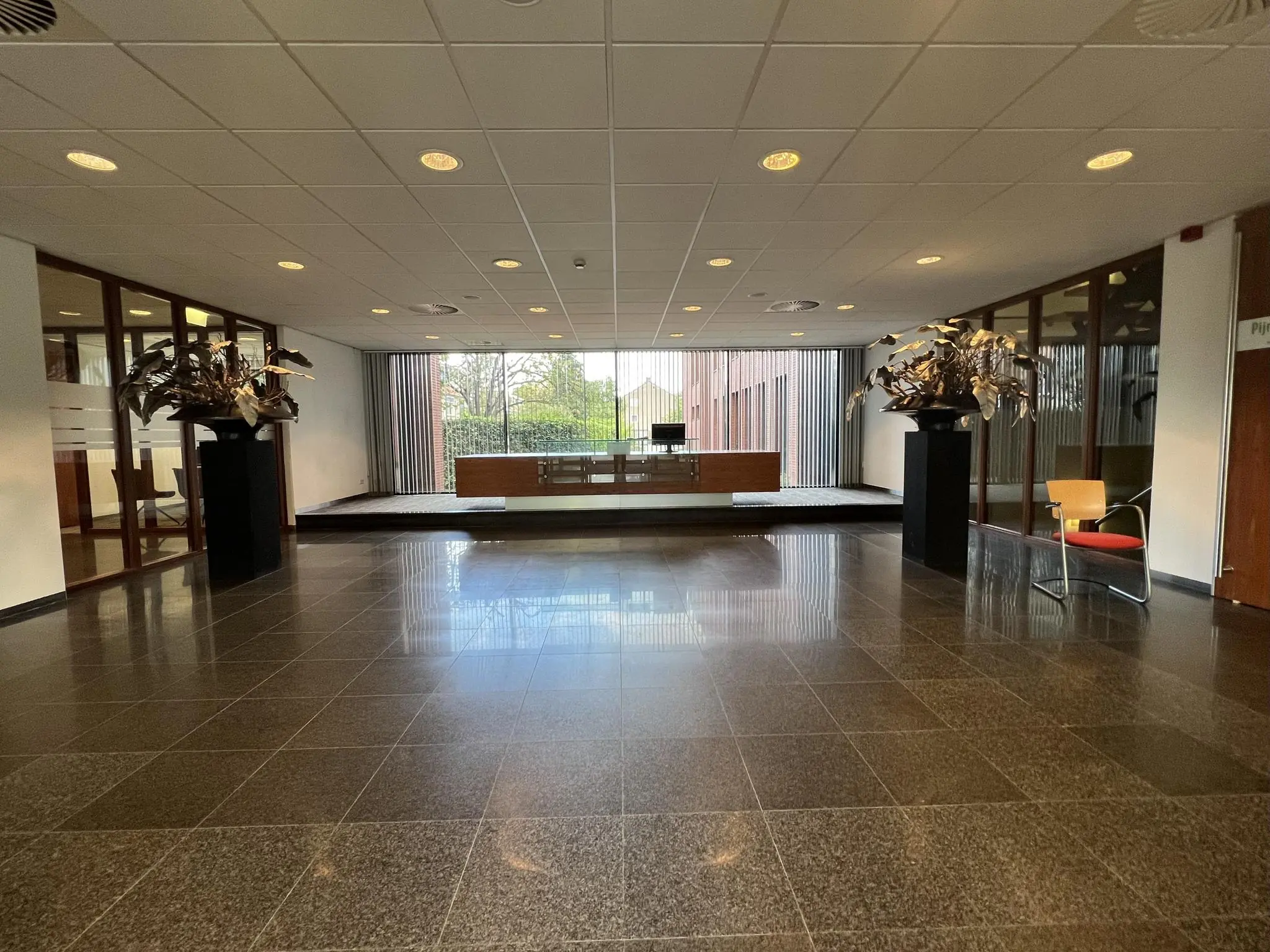 Moderne ontvangsthal aan de Groenekanseweg met glanzende tegelvloer, receptiebalie en metalen kunstobjecten.
