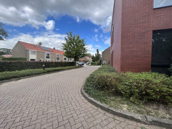 Straatbeeld van de Groenekanseweg met rijtjeshuizen links en een modern rood bakstenen gebouw rechts.