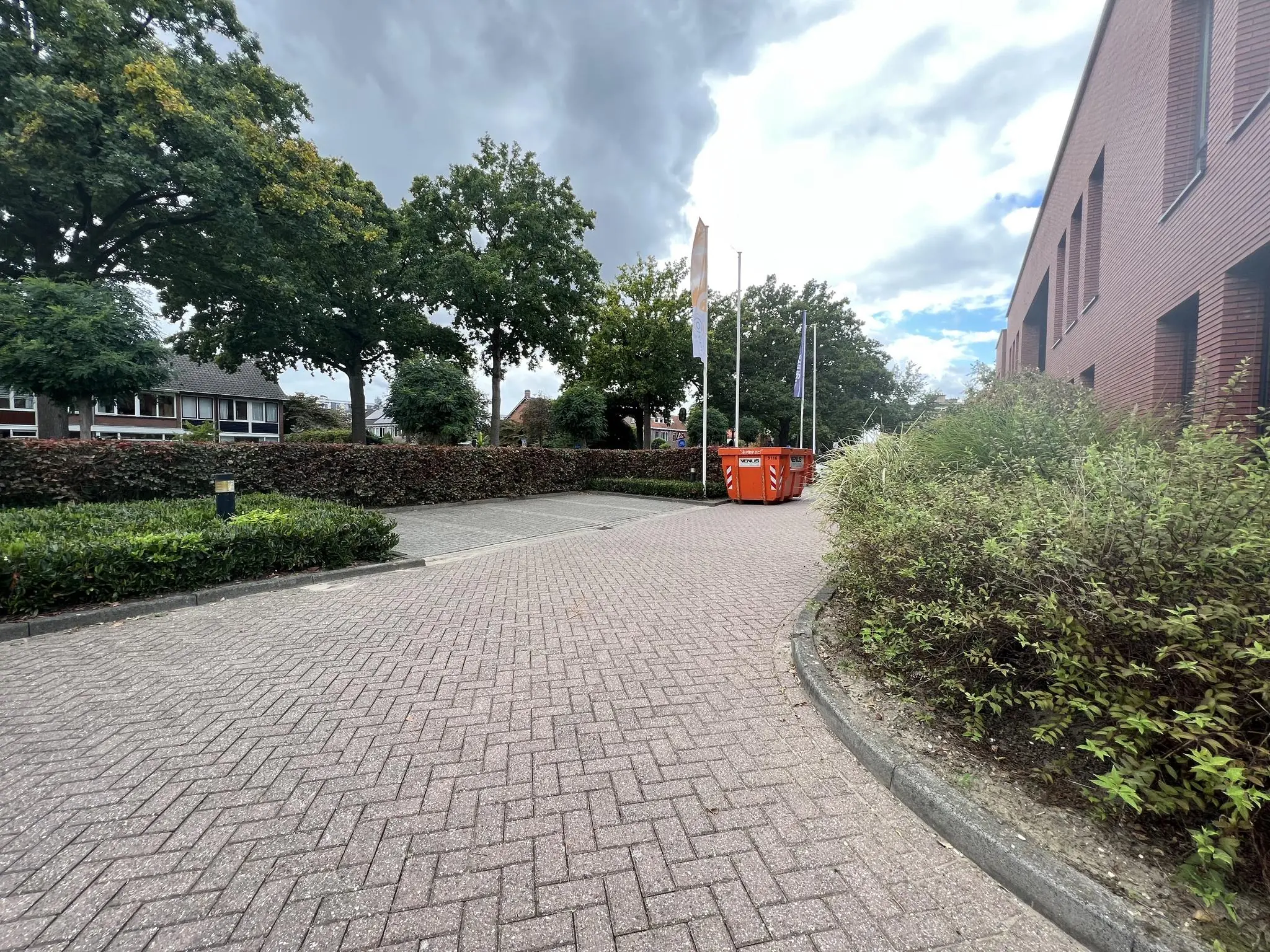 Gebogen straat aan de Groenekanseweg met rode afvalcontainers, bakstenen gebouw rechts en bomen aan de linkerkant.