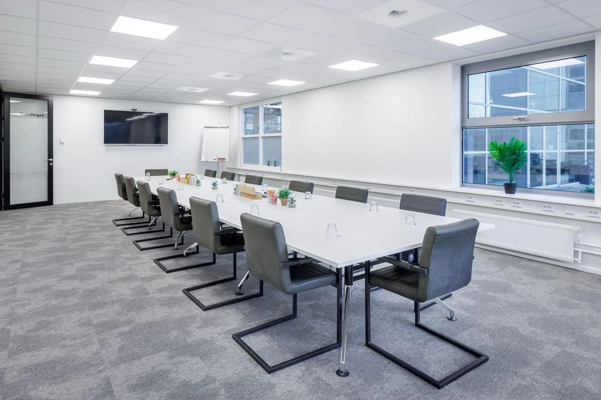 Moderne vergaderruimte aan de Spicalaan met een lange witte tafel, groene stoelen en een scherm aan de muur.