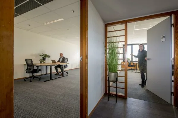 Vrouw opent deur naar modern kantoor aan de Fokkerstraat met man aan een bureau.