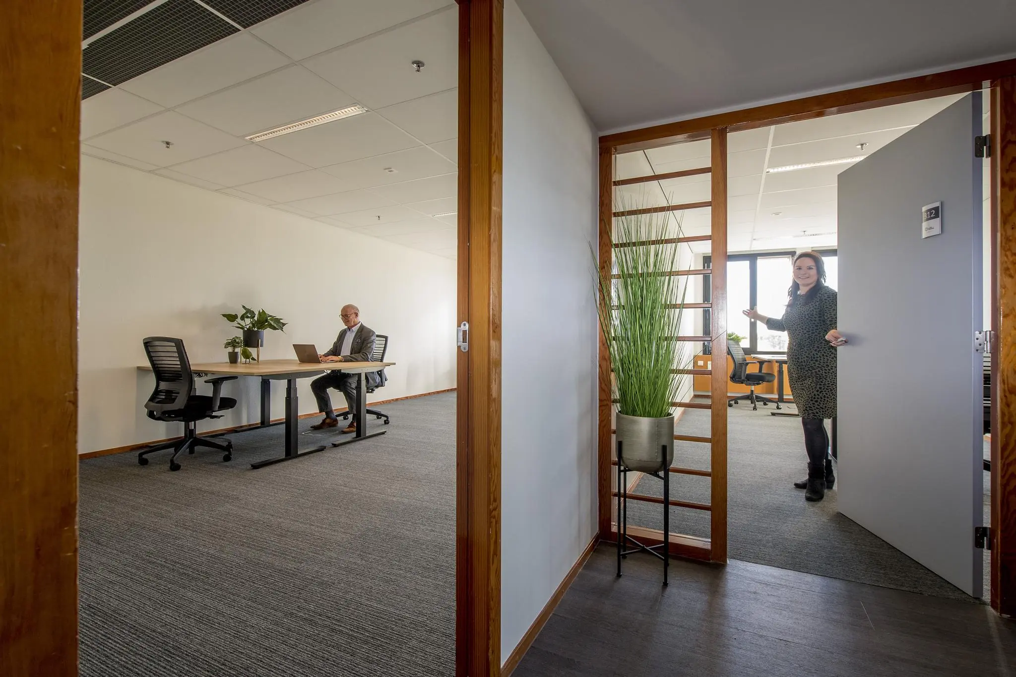 Vrouw opent deur naar modern kantoor aan de Fokkerstraat met man aan een bureau.