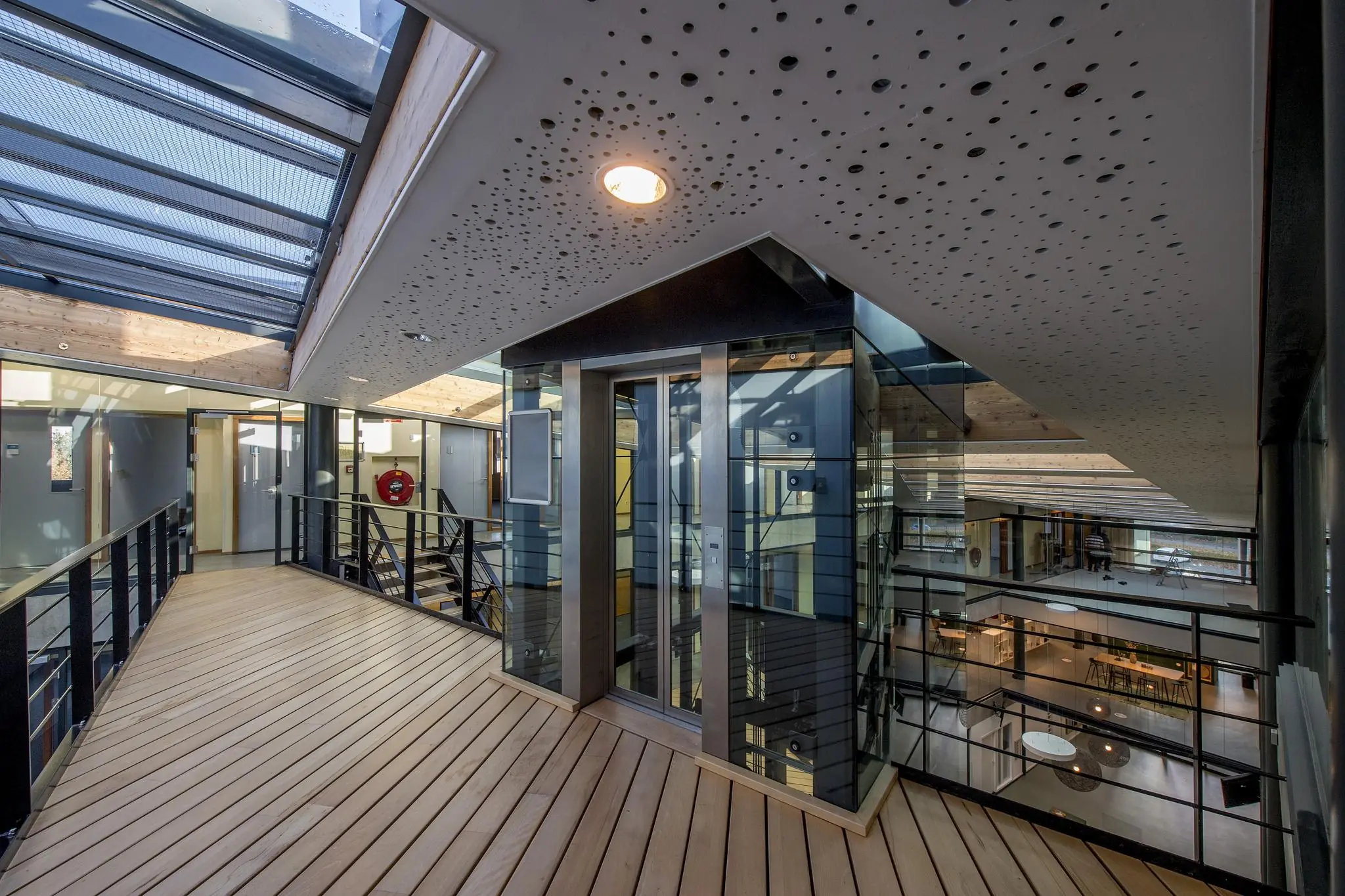 Moderne binnenruimte aan de Fokkerstraat met glazen lift, houten vloer en metalen balustrades.