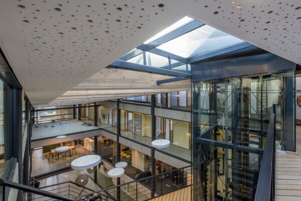 Modern kantoorgebouw aan de Fokkerstraat met glazen lift, open atrium en veel daglicht via een glazen dak.
