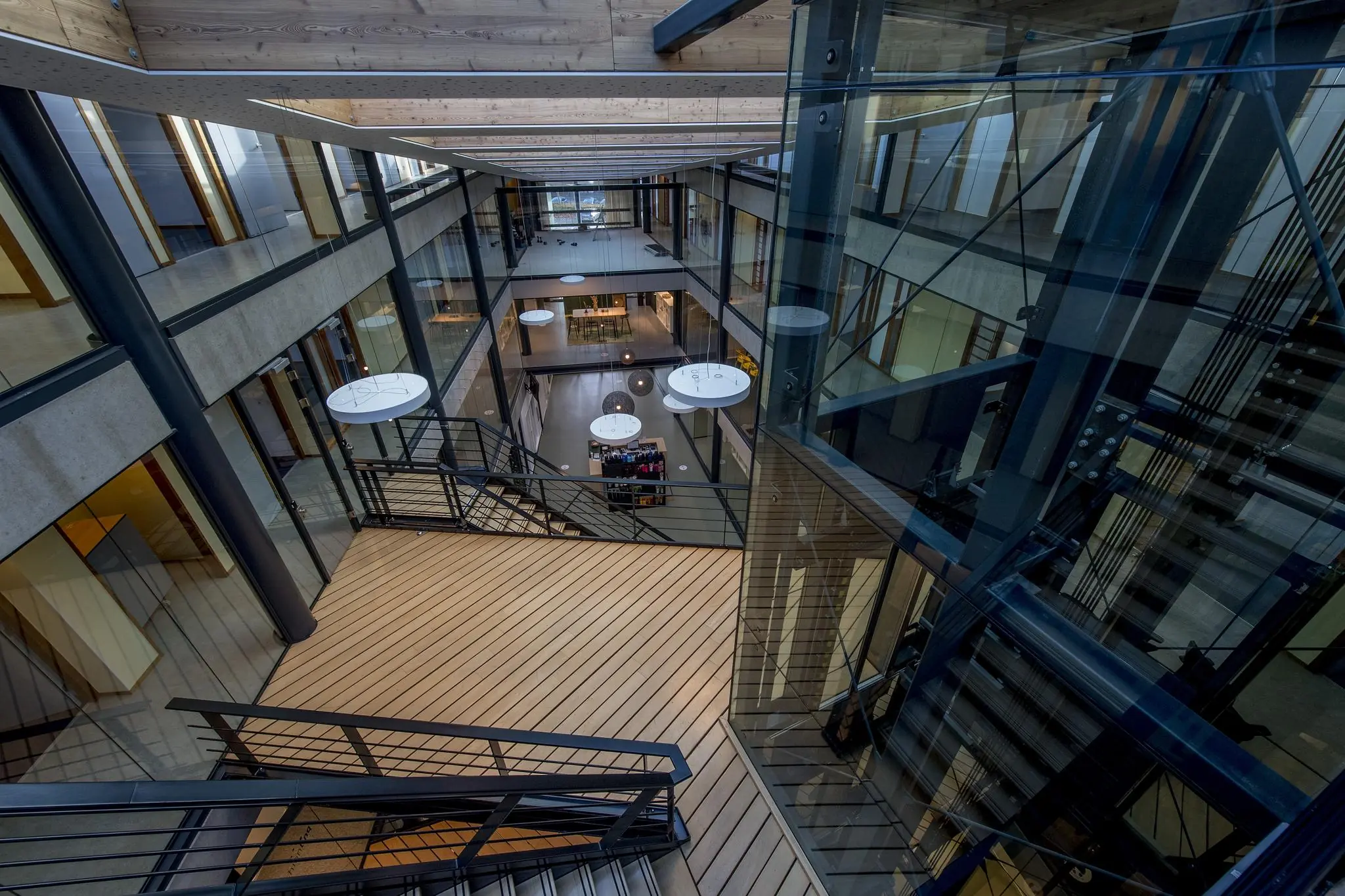 Modern interieur van een kantoorgebouw aan de Fokkerstraat met glazen wanden, houten vloeren en een centrale vide met zicht op meerdere verdiepingen.