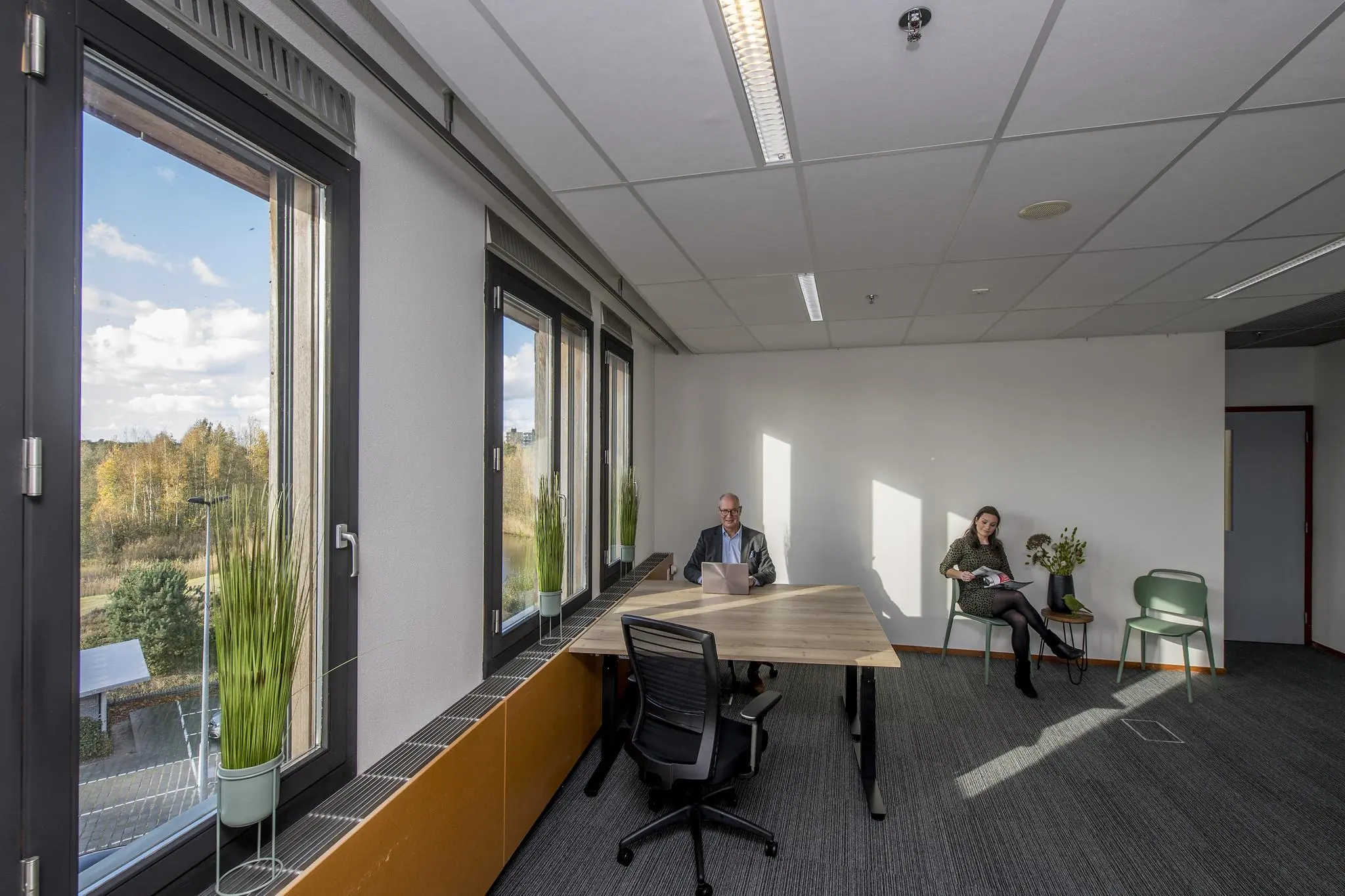Twee mensen in een licht kantoor aan de Fokkerstraat, met grote ramen en uitzicht op een groen landschap.