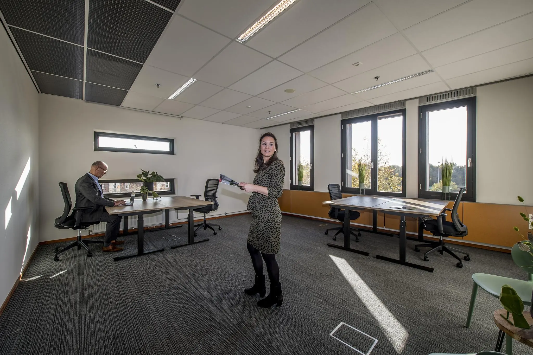 Twee mensen in een modern, licht kantoor aan de Fokkerstraat met meerdere bureaus en grote ramen.