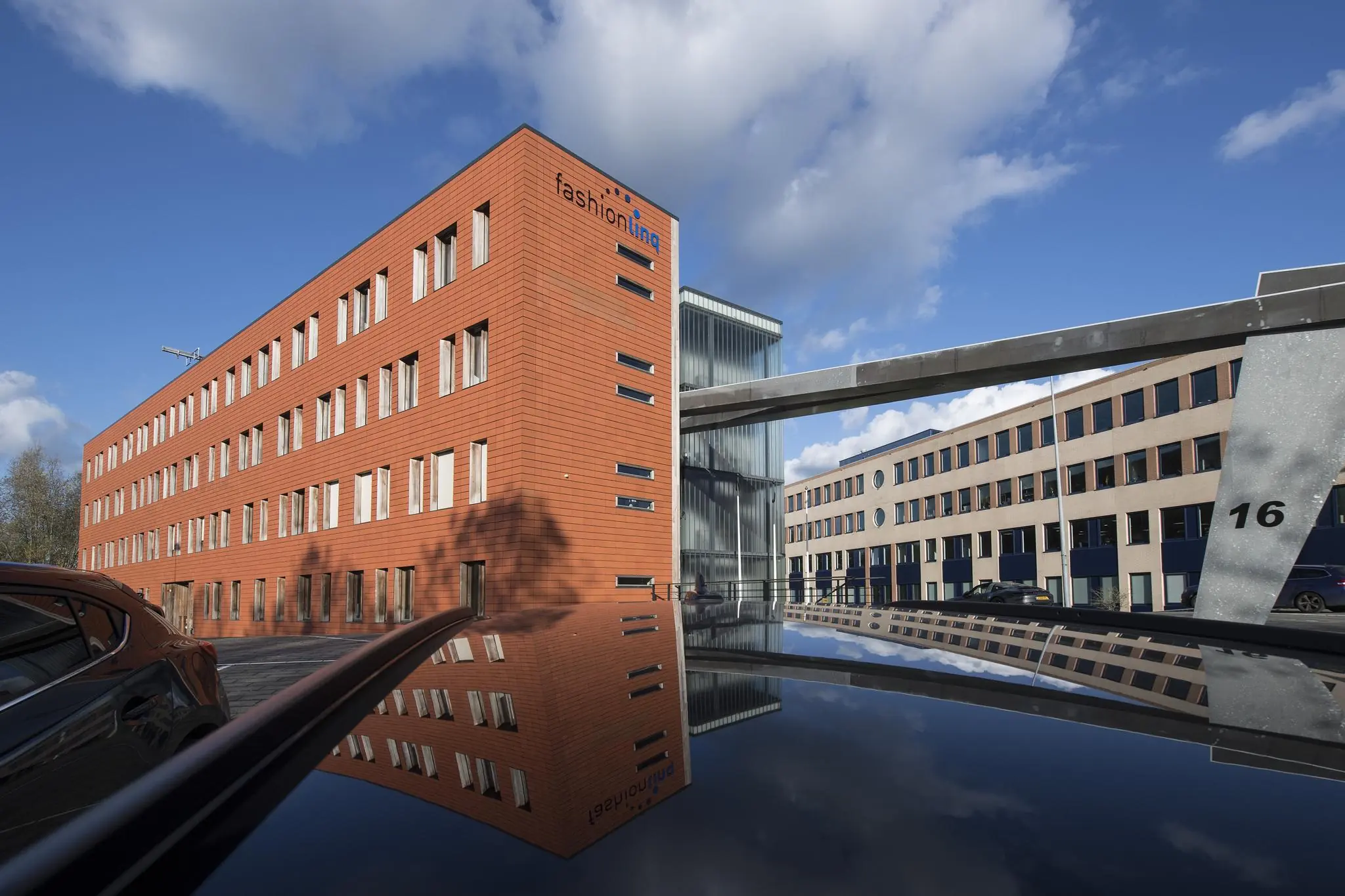 Bedrijfsgebouwen aan de Fokkerstraat in helder daglicht, met spiegeling van het rode Fashionlinq-pand op een auto.