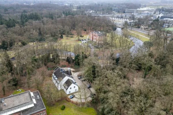 Luchtfoto van gebouwen aan de Driebergseweg te Zeist, omgeven door bos en een vijver.