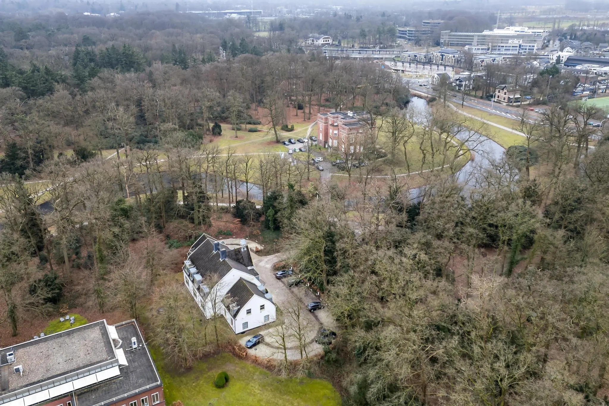 Luchtfoto van gebouwen aan de Driebergseweg te Zeist, omgeven door bos en een vijver.