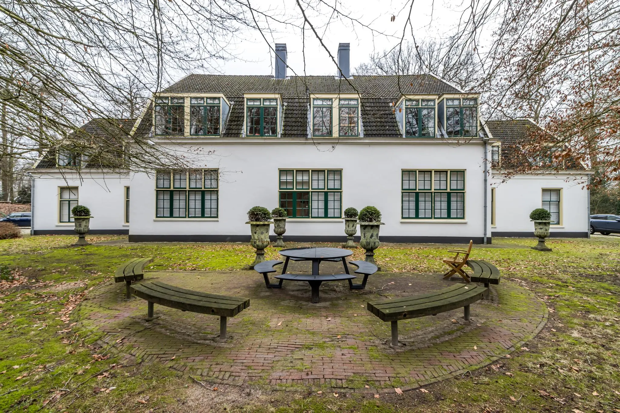 Witte villa aan de Driebergseweg met ronde picknicktafel en gebogen houten bankjes in een tuin met herfstbladeren.