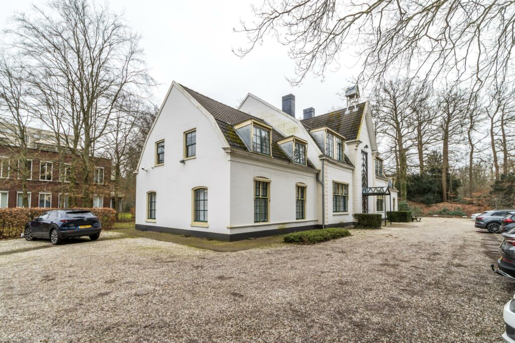 Wit landhuis aan de Driebergseweg met parkeerplaatsen op een grindterrein en omliggende bomen.