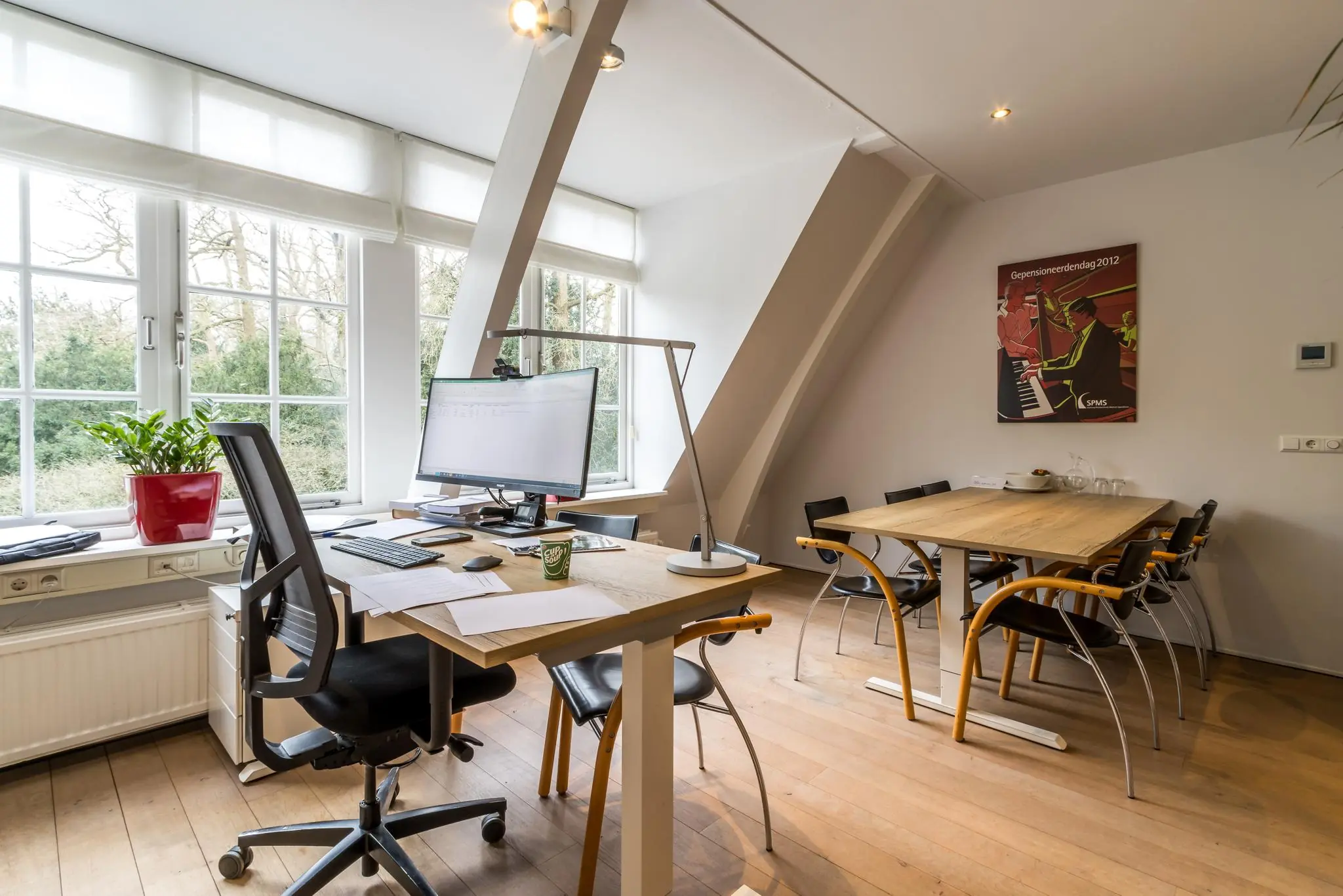 Modern kantoor met bureau aan het raam, vergadertafel met stoelen en een poster aan de muur.