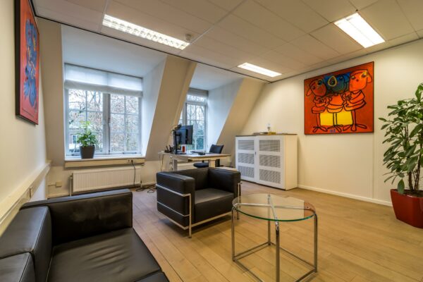 Modern kantoor met zitgedeelte, bureau bij het raam en kleurrijke kunst aan de muur aan de Driebergseweg.