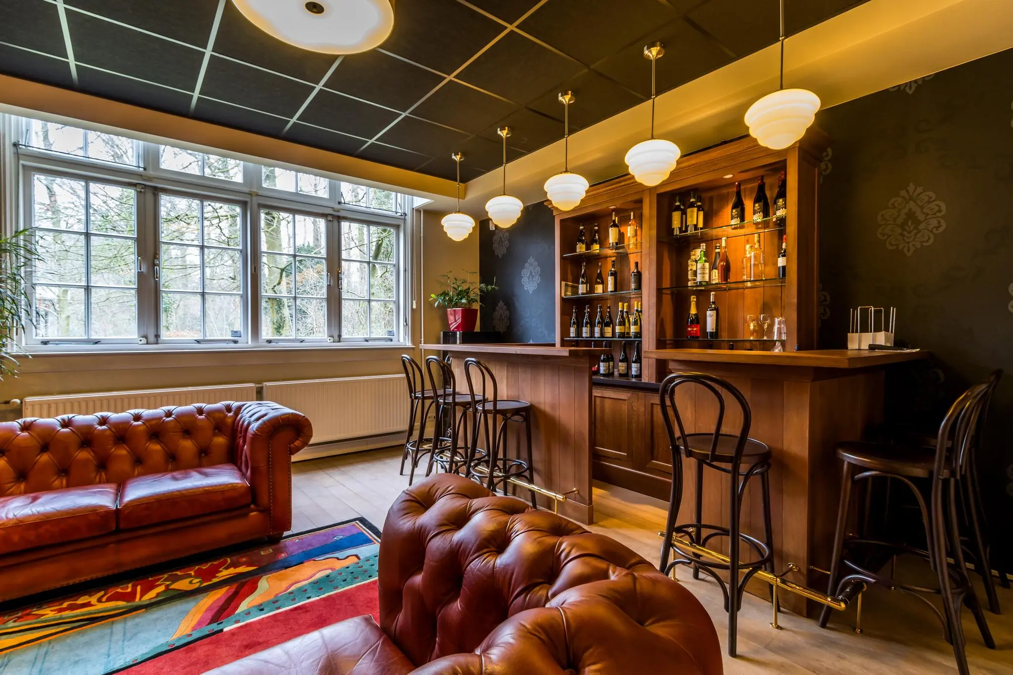 Sfeervolle huisbar aan de Driebergseweg met leren chesterfieldbanken, houten bar en flessenverzameling.